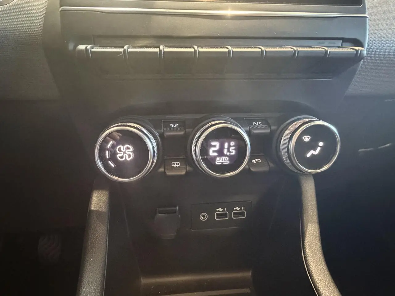 Gros plan sur les commandes de climatisation noires de la Renault Clio blanche, avec affichage digital à 21,5°C.