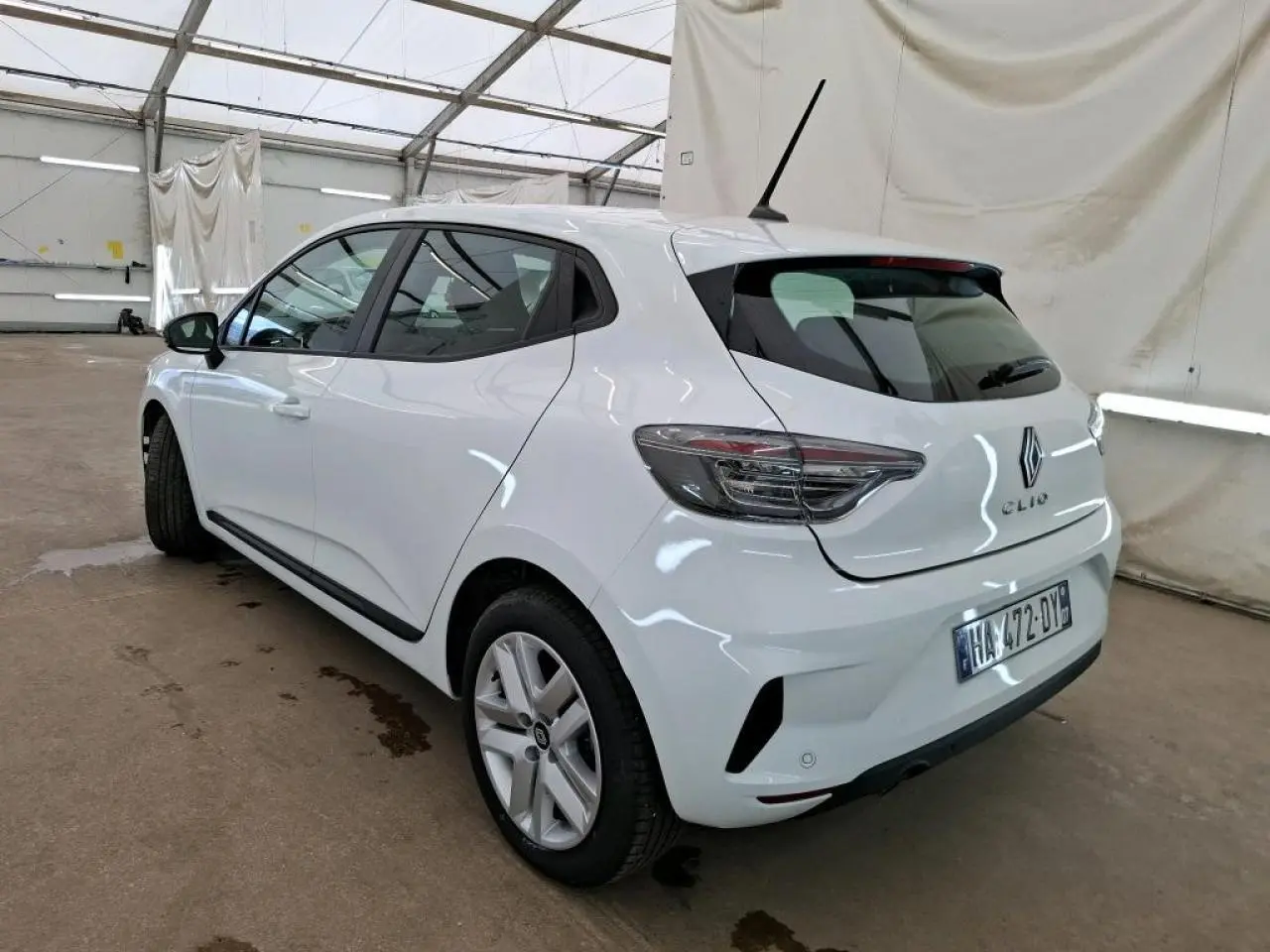 Renault Clio blanche vue 3/4 arrière droit, avec feux arrière LED et jantes alliage 16 pouces dans un garage.