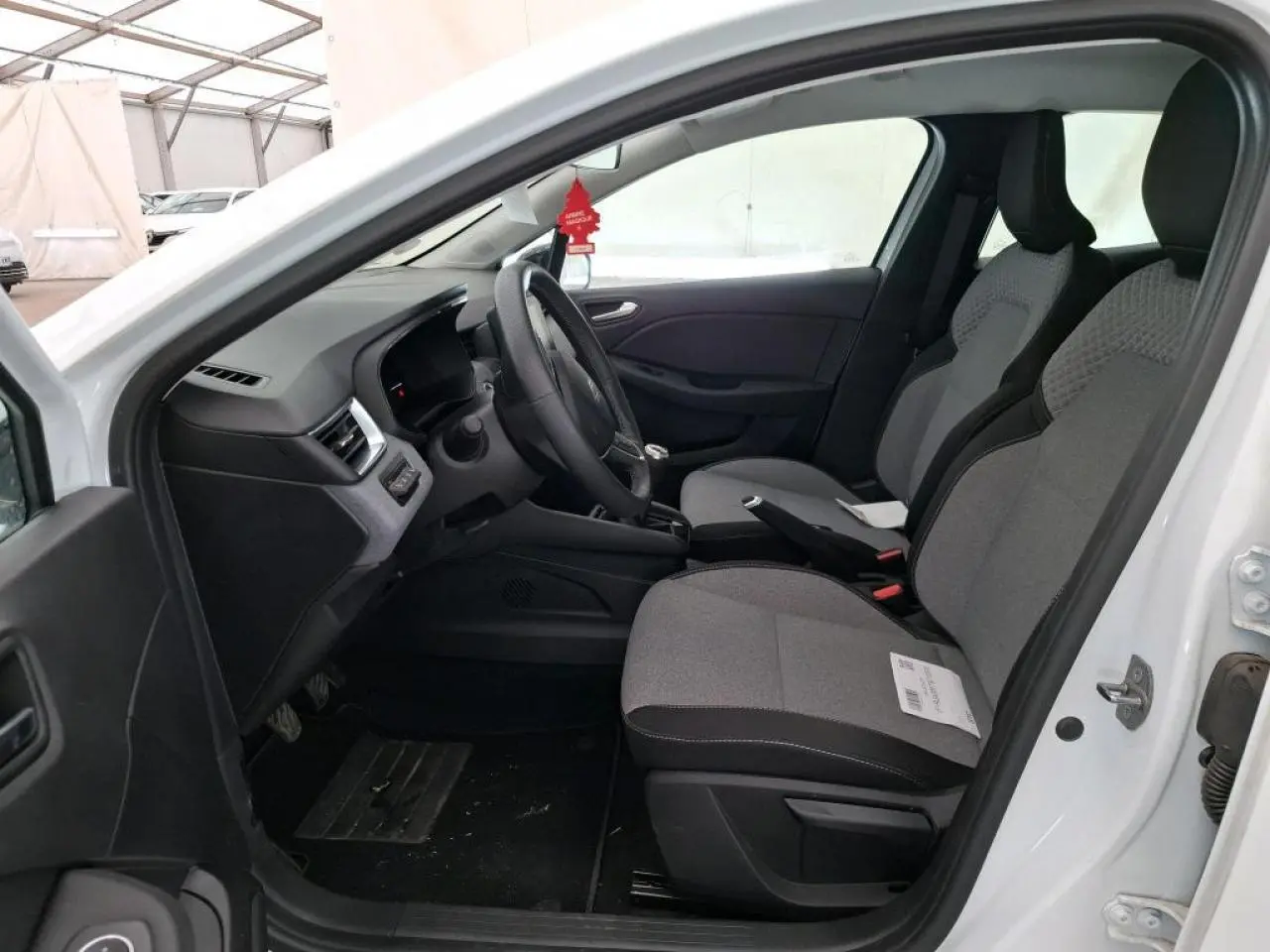 Vue intérieure côté conducteur de la Renault Clio blanche 2024, sièges tissu gris et volant multifonction.