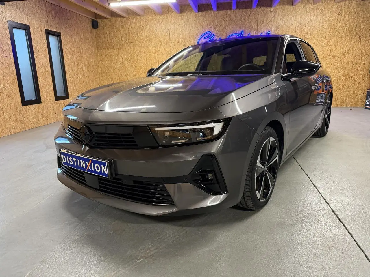 Opel Astra gris foncé vue 3/4 avant droit en intérieur, avec calandre noire et jantes alliage 17 pouces.
