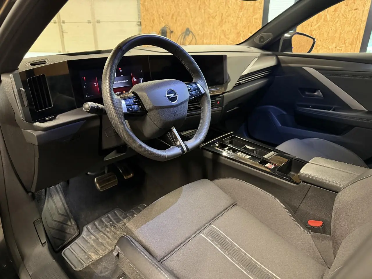Intérieur avant droit de l’Opel Astra 2024, montrant le volant cuir, tableau de bord digital et sellerie tissu gris foncé.