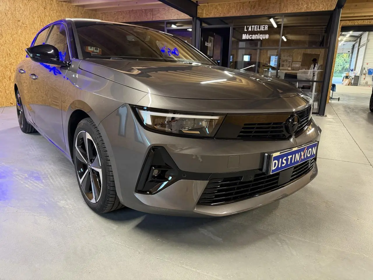 Opel Astra gris foncé vue 3/4 avant droit, calandre noire et jantes alliage 17 pouces diamantées.