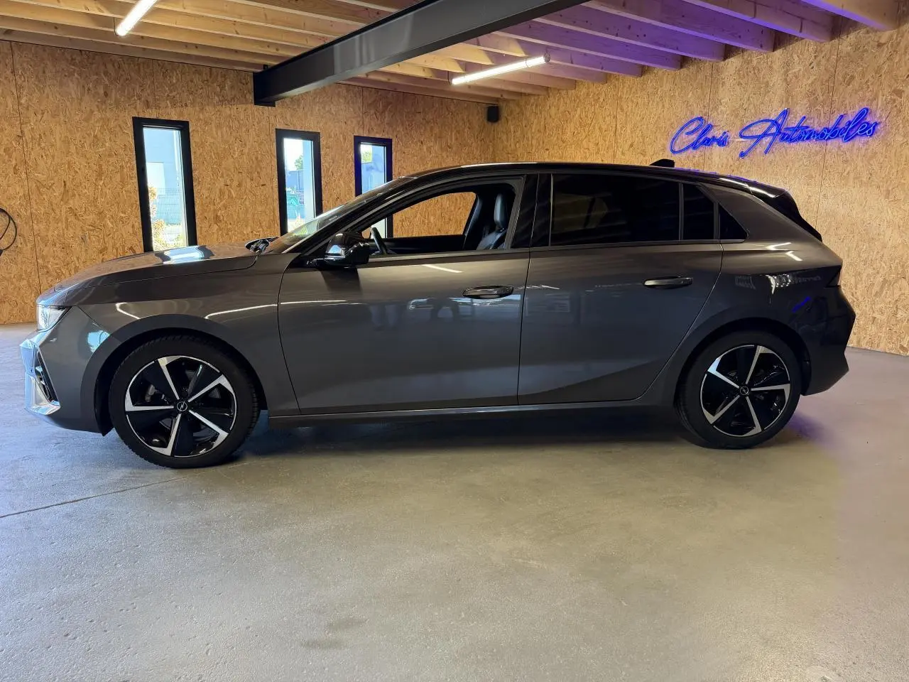 Opel Astra 2024 gris foncé vue de profil côté gauche, jantes alliage noires et vitres surteintées.