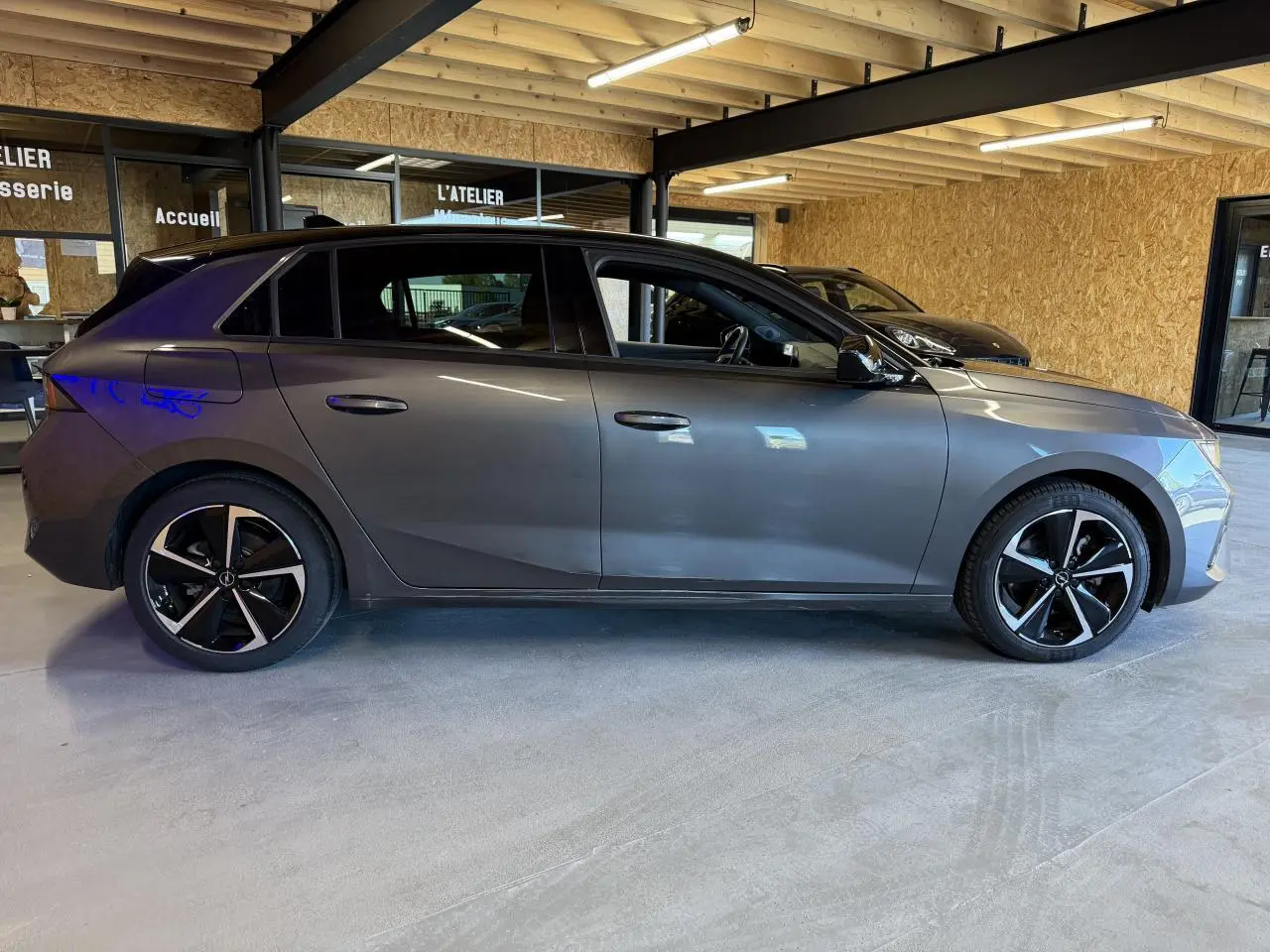 Vue latérale droite d'une Opel Astra gris foncé avec jantes alliage noires et toit noir dans un garage.
