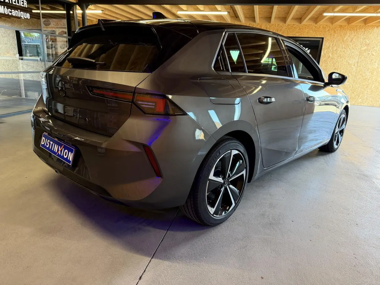 Vue 3/4 arrière droit d'une Opel Astra gris foncé avec toit noir et jantes alliage 17 pouces dans un garage.