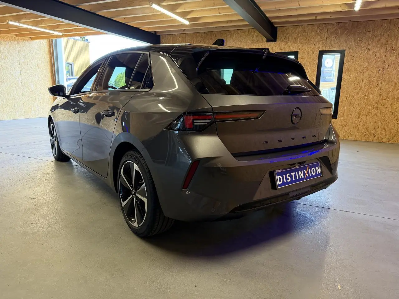 Vue 3/4 arrière droite de l'Opel Astra gris foncé avec jantes alliage 17 pouces et toit noir Karbon dans un garage.
