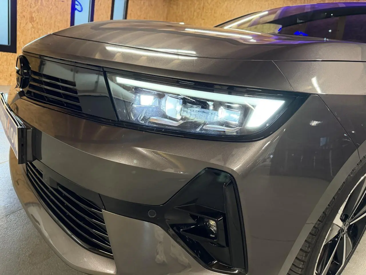Gros plan sur l'avant droit d'une Opel Astra gris foncé avec phares LED et calandre noire brillante.