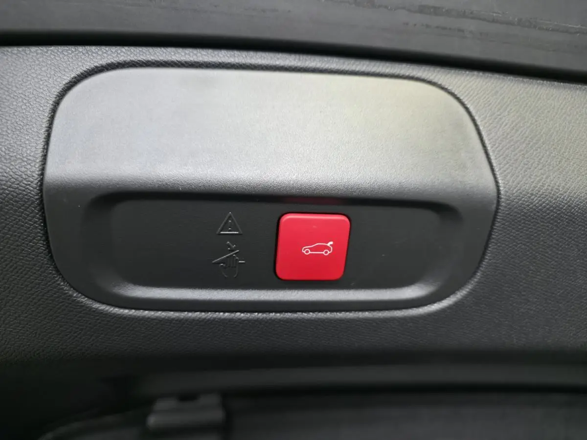 Bouton rouge d'ouverture électrique du hayon sur panneau intérieur noir d'une Peugeot 408 gris 2024 Berline GT hybride rechargeable