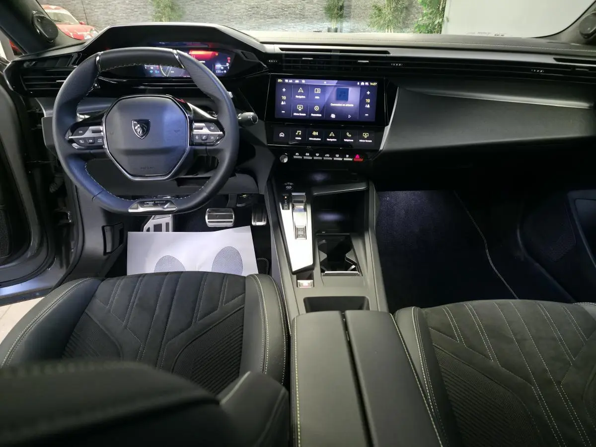 Intérieur avant du Peugeot 408 2024 avec tableau de bord numérique, volant cuir perforé et console centrale moderne.