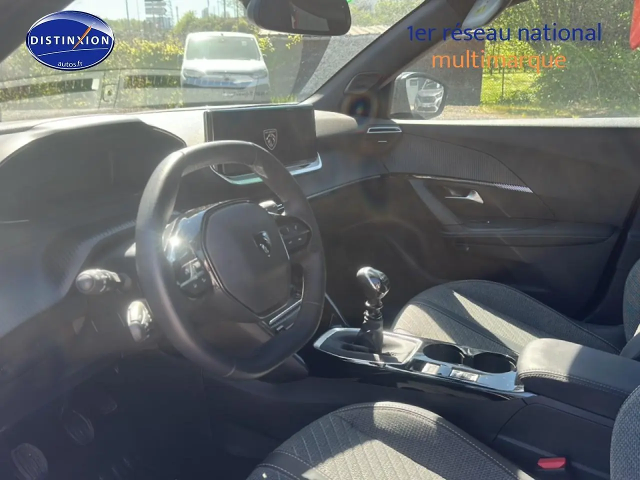 Vue intérieure côté conducteur du Peugeot 2008 1.2 100 Allure 2025 avec volant multifonction et sellerie tissu gris.