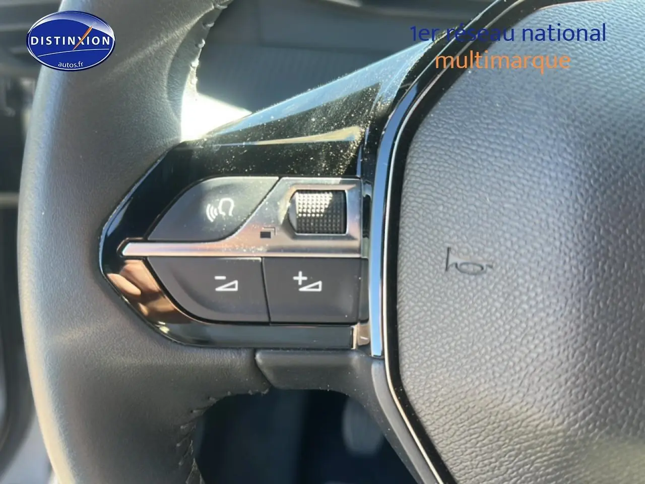 Gros plan sur les commandes gauche du volant noir du Peugeot 2008 1.2 100 Allure gris Artense, avec boutons multifonctions.