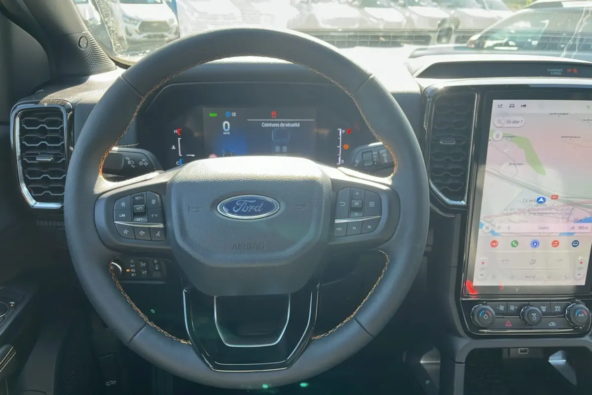 Vue intérieure centrée sur le volant cuir du Ford Ranger PHEV 281 Wildtrak, avec écran tactile GPS et commandes multifonctions visibles.