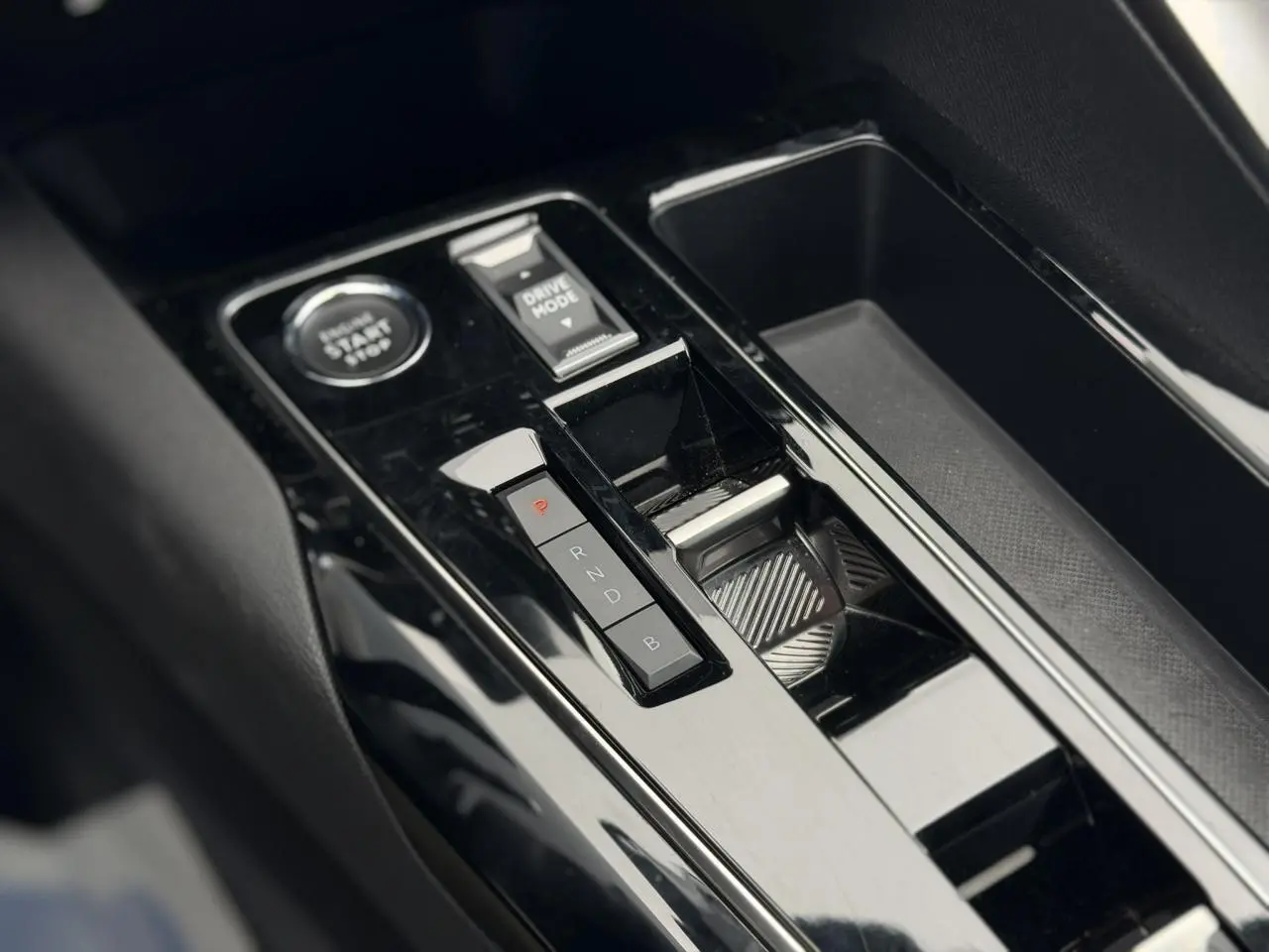 Gros plan sur la console centrale noire brillante du Peugeot 3008 Plug-in Hybrid avec sélecteur de mode et bouton start/stop.