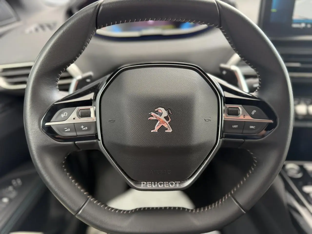 Volant cuir noir Mistral avec logo Peugeot au centre, vue frontale du poste de conduite du 3008 Plug-in Hybrid 2024.