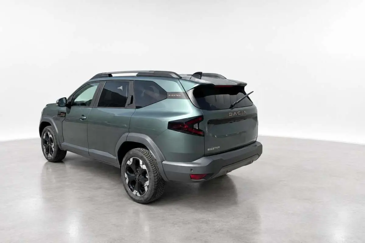 Vue 3/4 arrière gauche du Dacia Bigster vert cèdre avec jantes alu noires et barres de toit modulables.