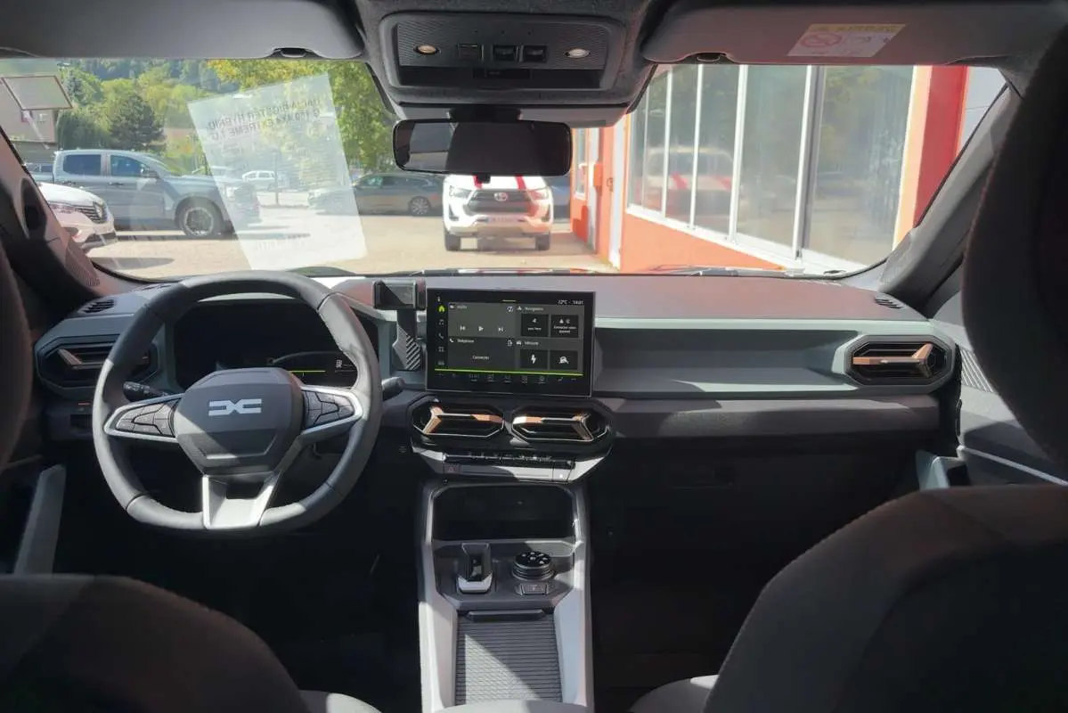 Vue intérieure avant du tableau de bord du Dacia Bigster vert cèdre avec écran tactile et volant multifonction.