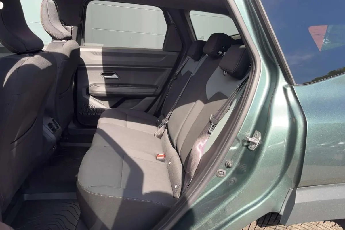 Vue latérale droite sur l'intérieur arrière du Dacia Bigster vert cèdre, montrant la banquette trois places et les finitions tissu.