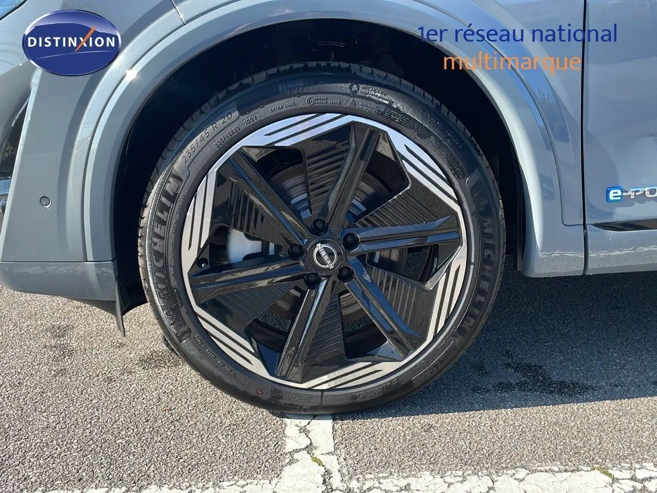 Gros plan sur l'avant droit du Nissan Qashqai gris céramique, mettant en valeur le phare LED et la jante noire à motifs blancs.