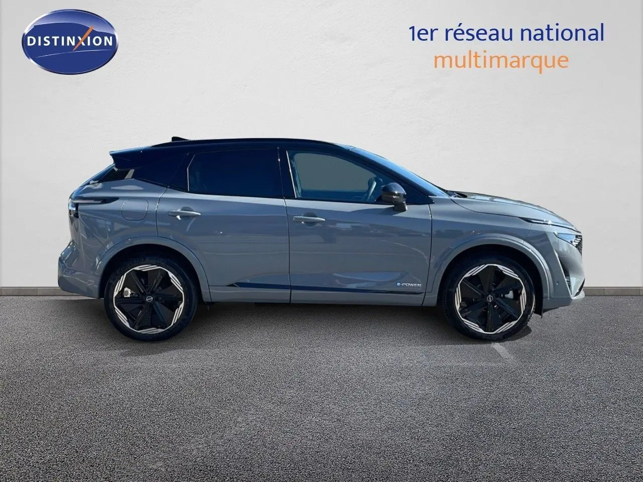 Nissan Qashqai gris céramique métal vu en 3/4 avant droit avec phares allumés et calandre noire distinctive.