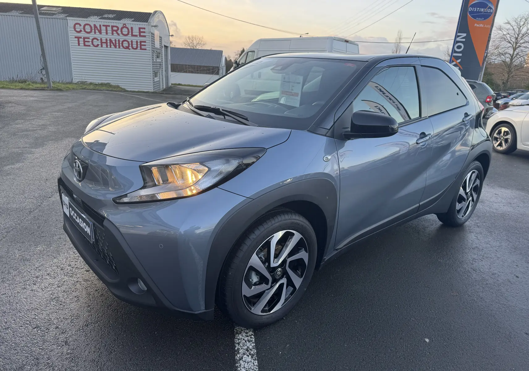 Toyota Aygo X bleu vue 3/4 avant droit avec phares allumés, roues alliage et carrosserie compacte cinq portes.