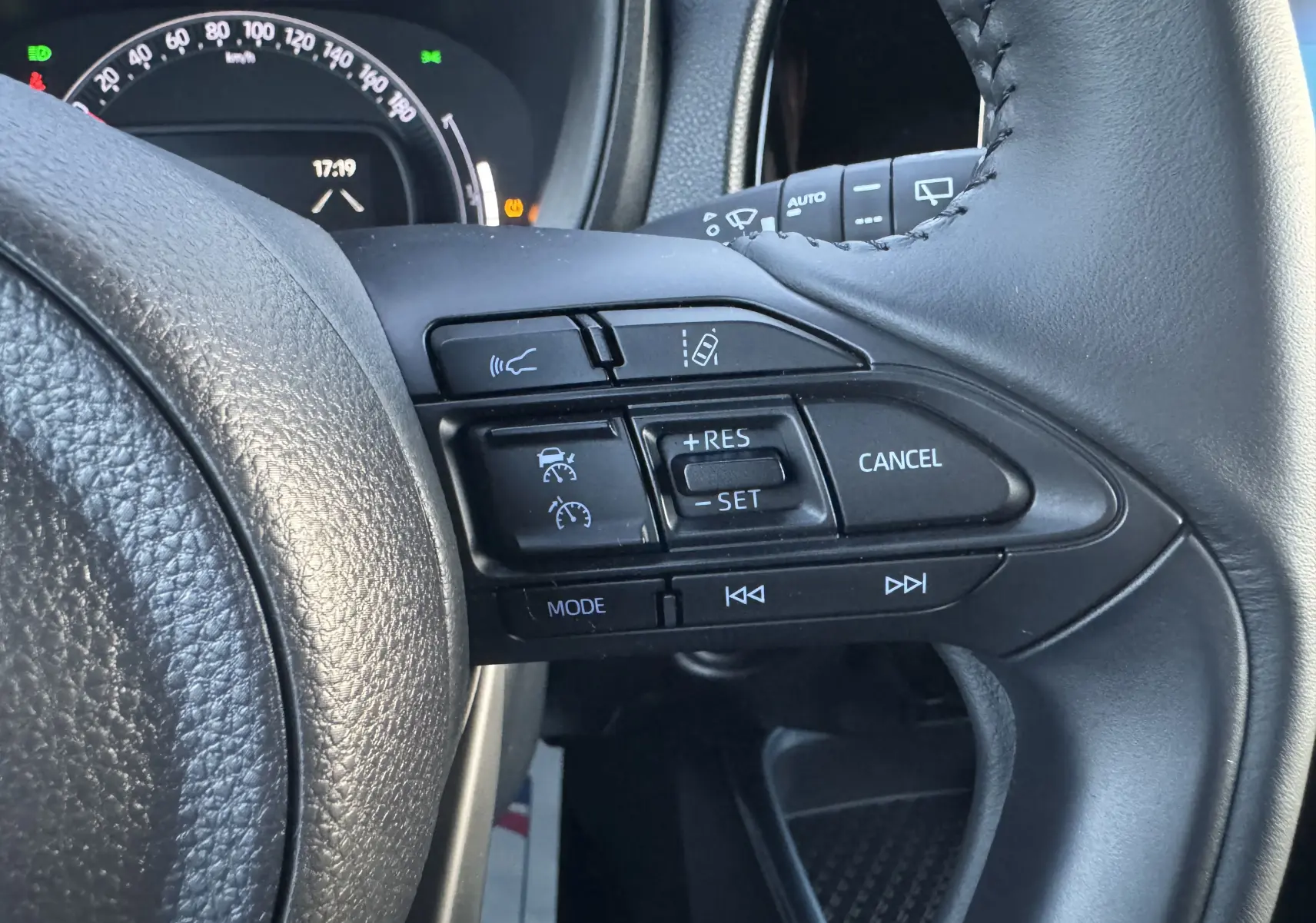 Gros plan sur les commandes au volant à droite du Toyota Aygo X bleu 2025, avec régulateur de vitesse et fonctions multimédia.