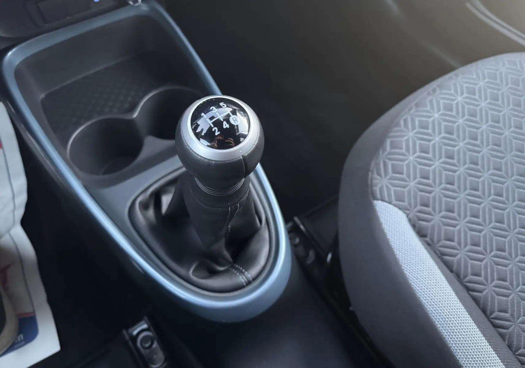 Gros plan sur le levier de vitesses manuel et la console centrale bleu de la Toyota Aygo X 2025, siège tissu gris visible.