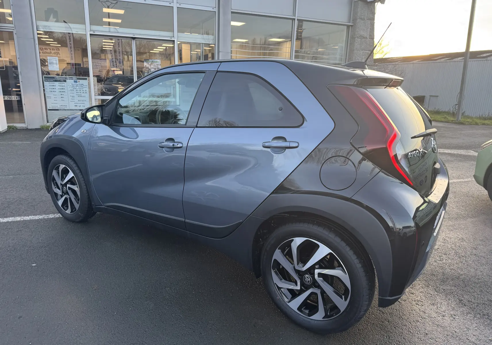 Vue 3/4 arrière droite d'une Toyota Aygo X 2025 bleu avec toit noir et feux arrière en forme de boomerang.