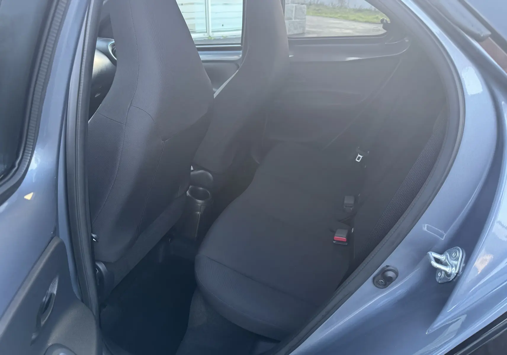 Vue intérieure côté droit sur la banquette arrière noire d'une Toyota Aygo X 2025 bleu, porte arrière ouverte.