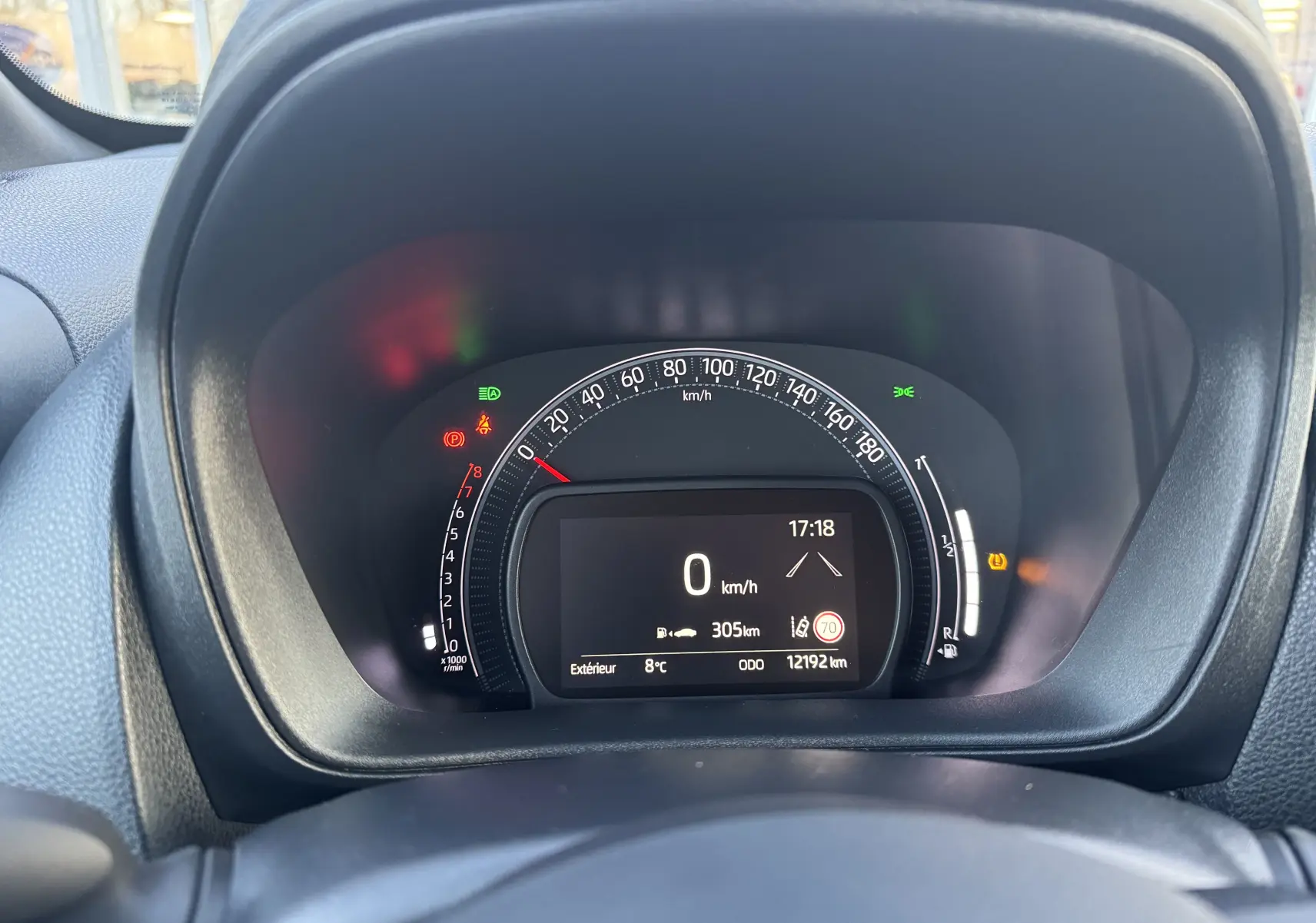 Vue rapprochée du tableau de bord numérique de la Toyota Aygo X 2025, affichant la vitesse à 0 km/h et divers voyants allumés.