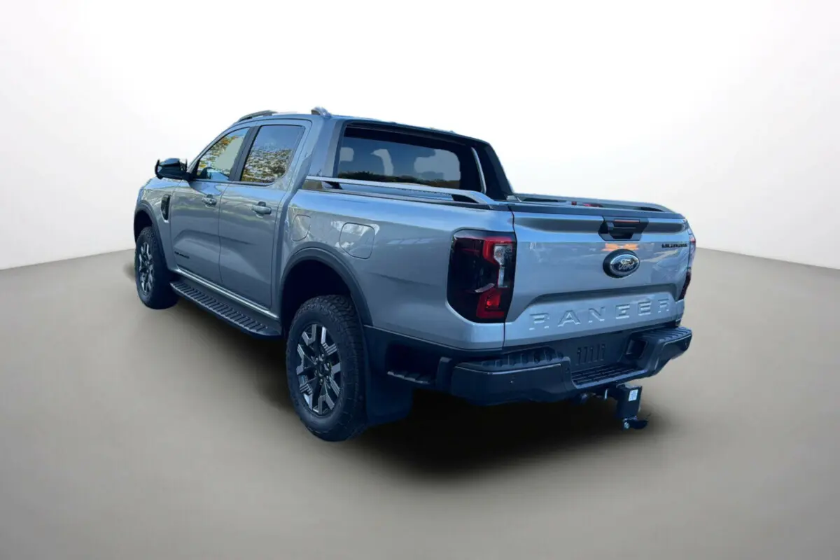 Ford Ranger PHEV gris iconic en 3/4 arrière droit, avec attelage et barres de toit visibles.