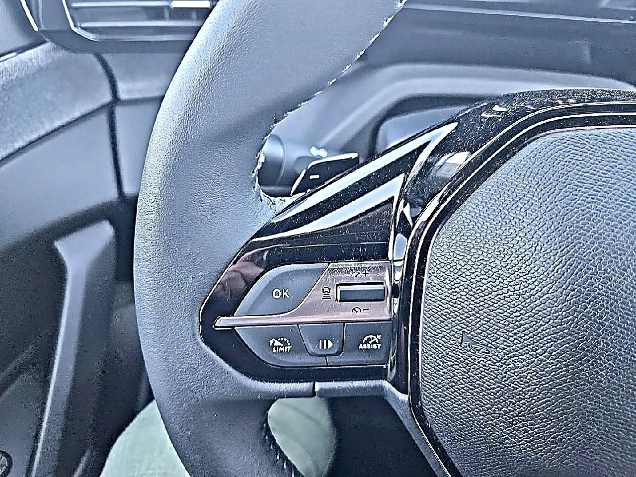 Gros plan sur le côté gauche du volant noir de la Peugeot 308 SW 2025 avec commandes multifonctions intégrées.