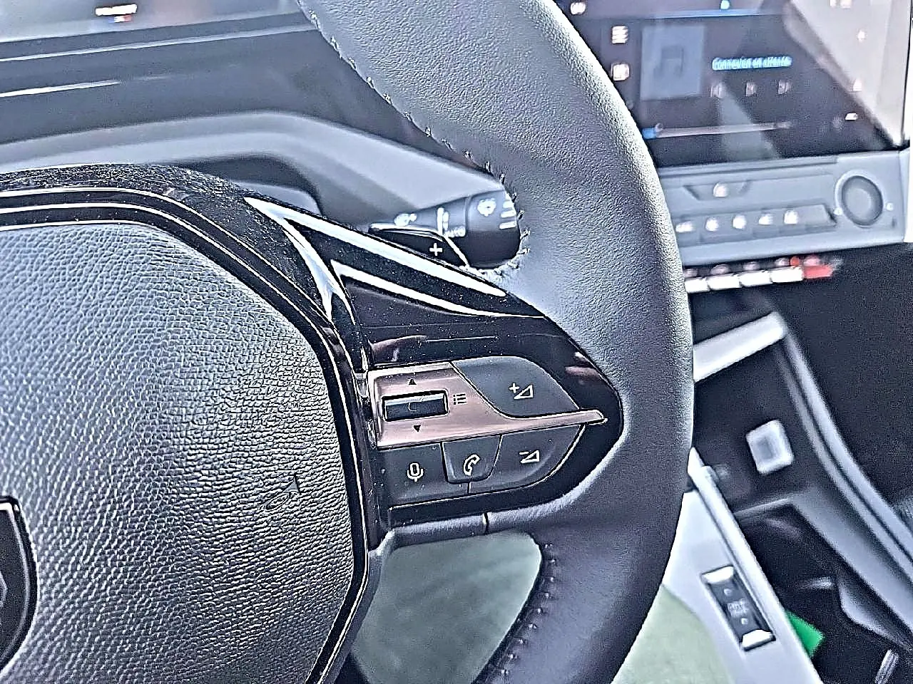 Gros plan sur le volant multifonction noir de la Peugeot 308 SW 1.5 BlueHDi 130 Allure gris Artense, avec commandes audio visibles.