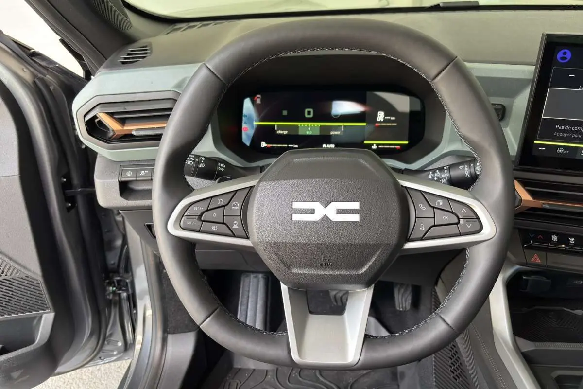 Vue intérieure centrée sur le volant cuir noir du Dacia Bigster Hybrid-G 150, avec tableau de bord digital et écran tactile.