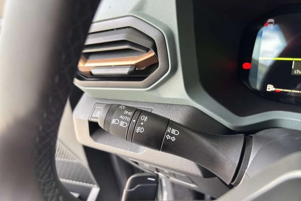 Gros plan sur la commande des phares et clignotants à gauche du volant dans le tableau de bord gris du Dacia Bigster Hybrid-G 150.