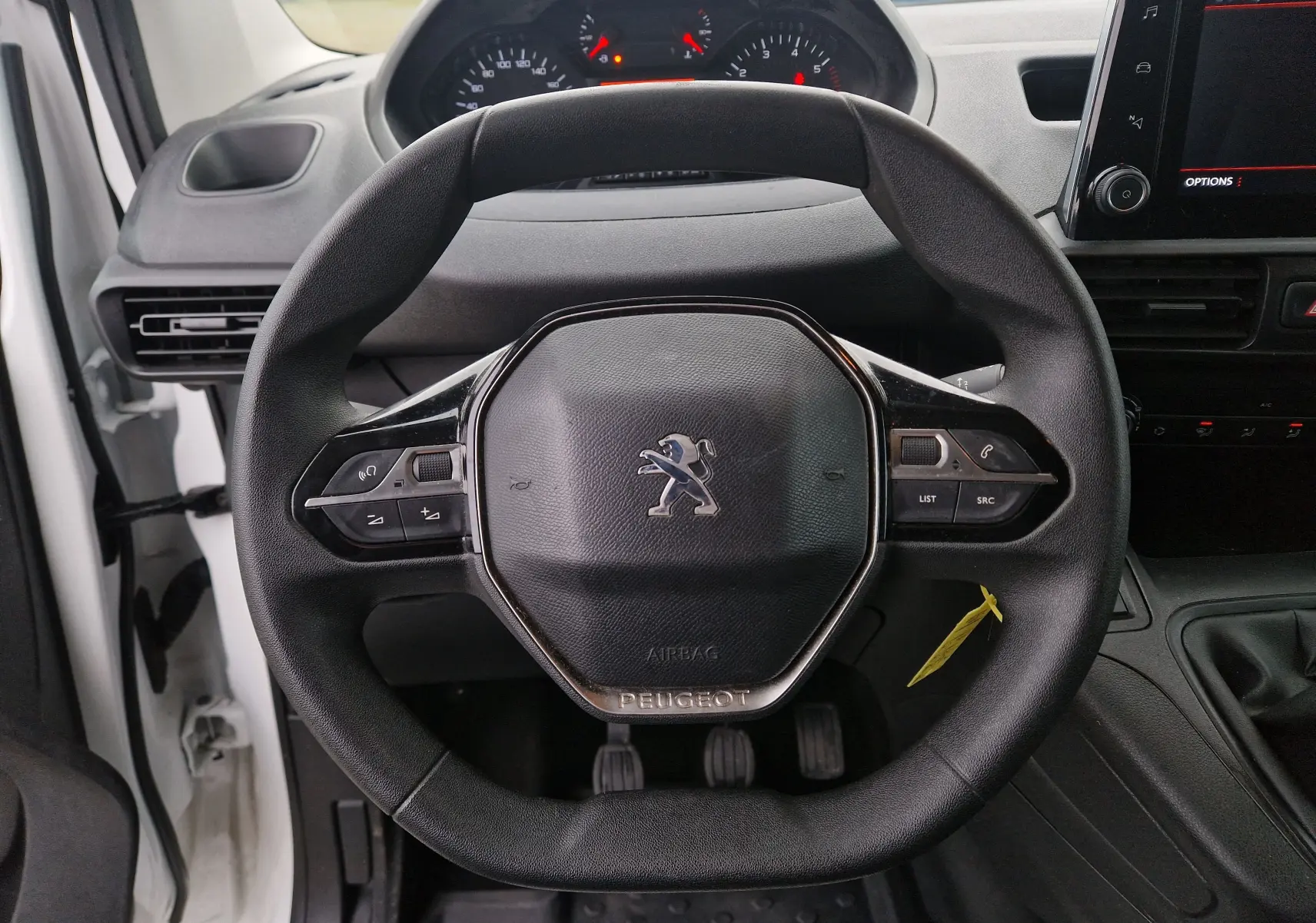 Vue rapprochée du volant noir du Peugeot Partner blanc 2020, avec commandes intégrées et tableau de bord visible en arrière-plan.