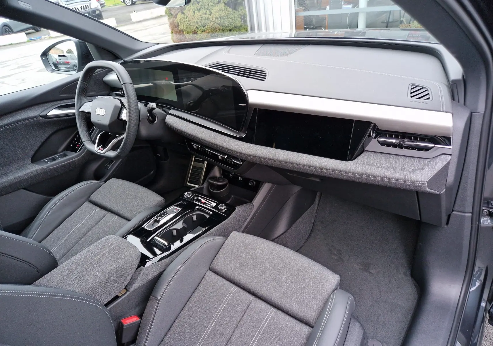 Vue intérieure côté conducteur de l'Audi Q6 e-tron Performance S-Line 2025 avec tableau de bord numérique et sellerie gris Manhattan.