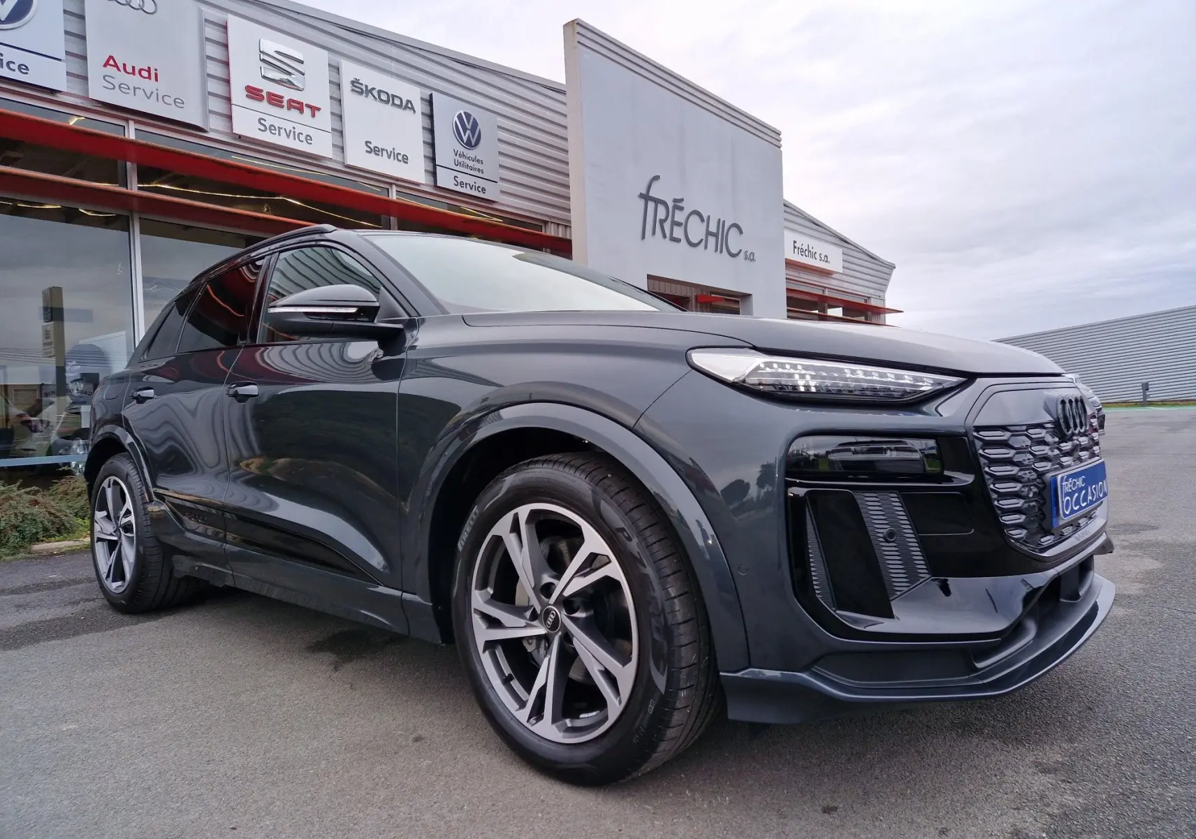 Vue 3/4 avant droite de l'Audi Q6 e-tron Performance S-Line gris Manhattan avec calandre noire et jantes sport.