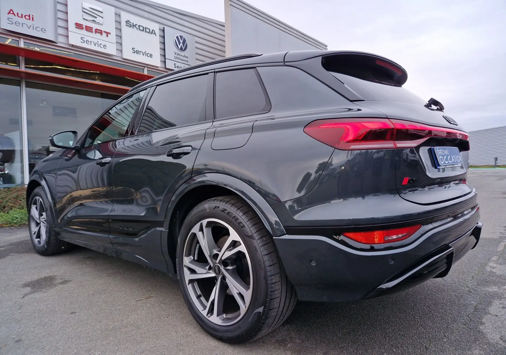 Vue 3/4 arrière droite d’un Audi Q6 e-tron Performance S-Line gris Manhattan avec jantes sport et feux LED distinctifs.