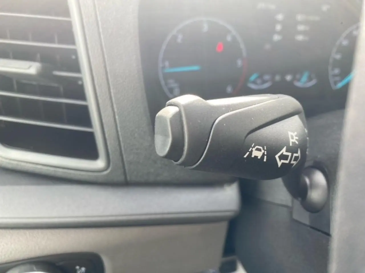 Gros plan sur la commande de clignotant avec fonction d’alerte de franchissement de ligne dans l’habitacle du Ford Transit blanc.
