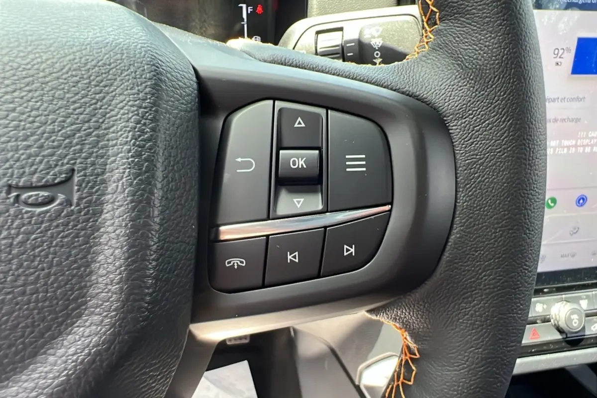 Gros plan sur les commandes multifonctions à droite du volant cuir noir du Ford Ranger Wildtrak PHEV 2025, avec surpiqûres orange.