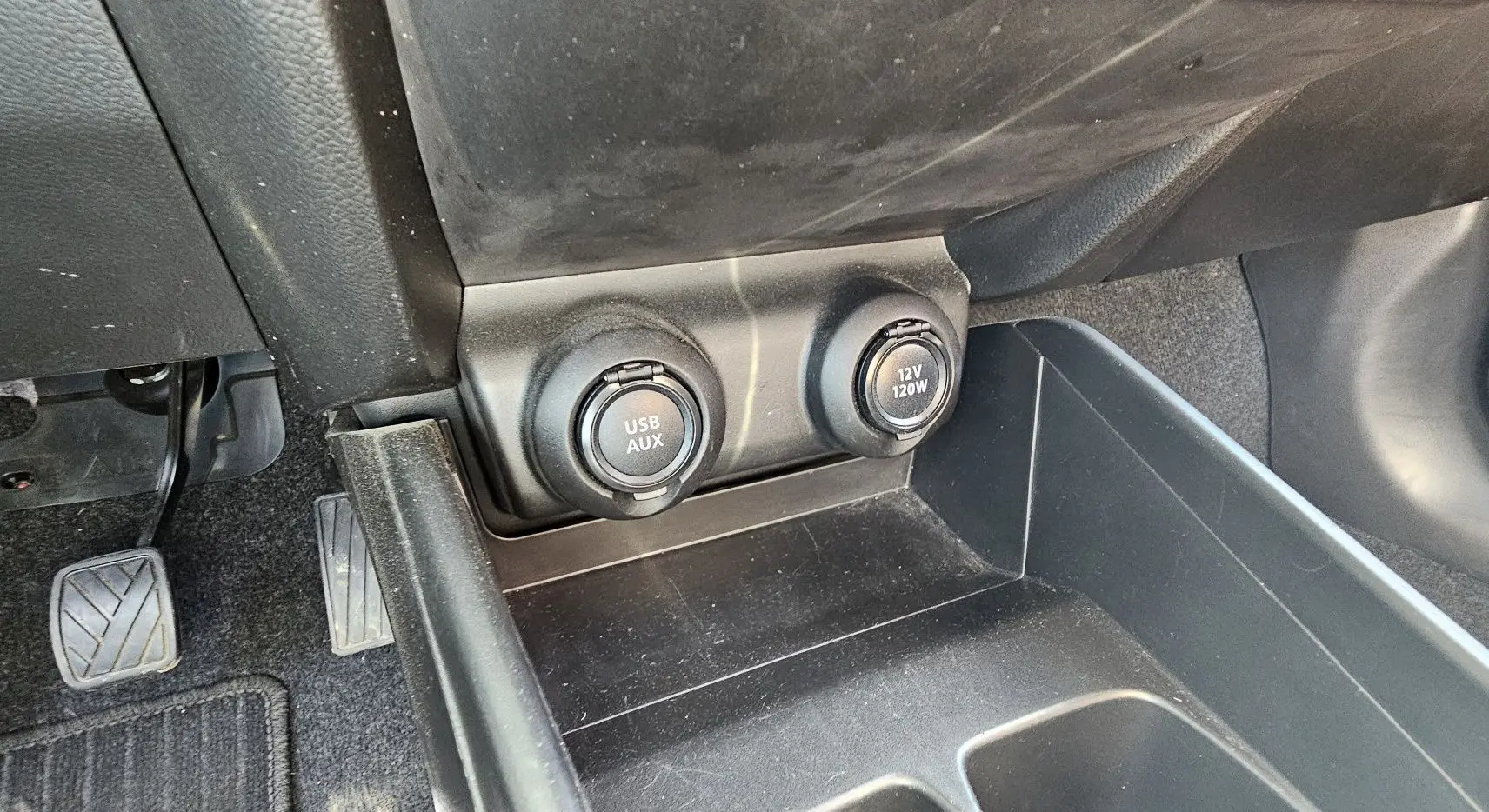 Vue rapprochée de la console centrale avant de la Suzuki Swift 2023 montrant les prises USB/AUX et 12V sous le tableau de bord.