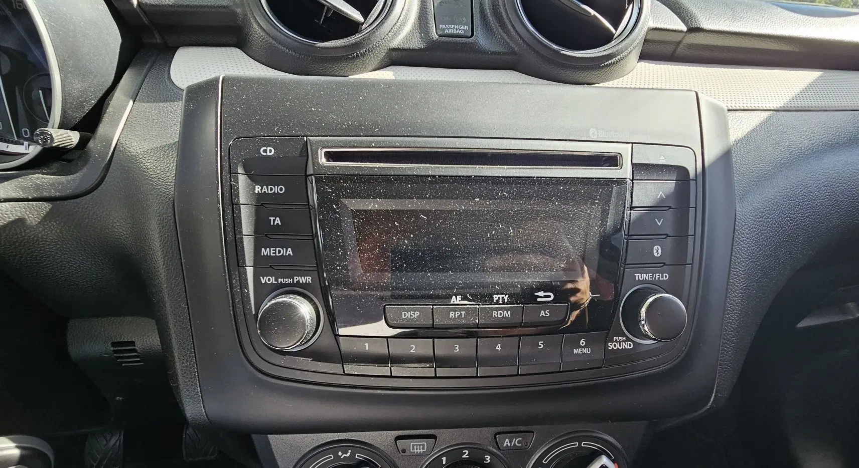 Gros plan sur la console centrale noire de la Suzuki Swift 2023, avec radio et commandes climatisation visibles.