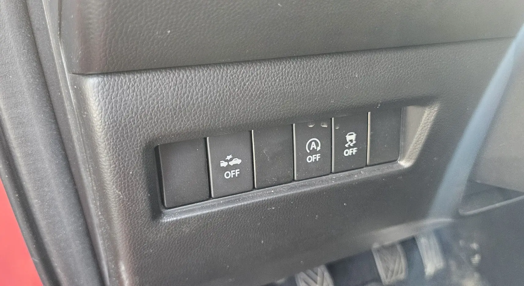 Gros plan sur les boutons de contrôle d'assistance à la conduite dans une Suzuki Swift rouge, intérieur noir texturé.
