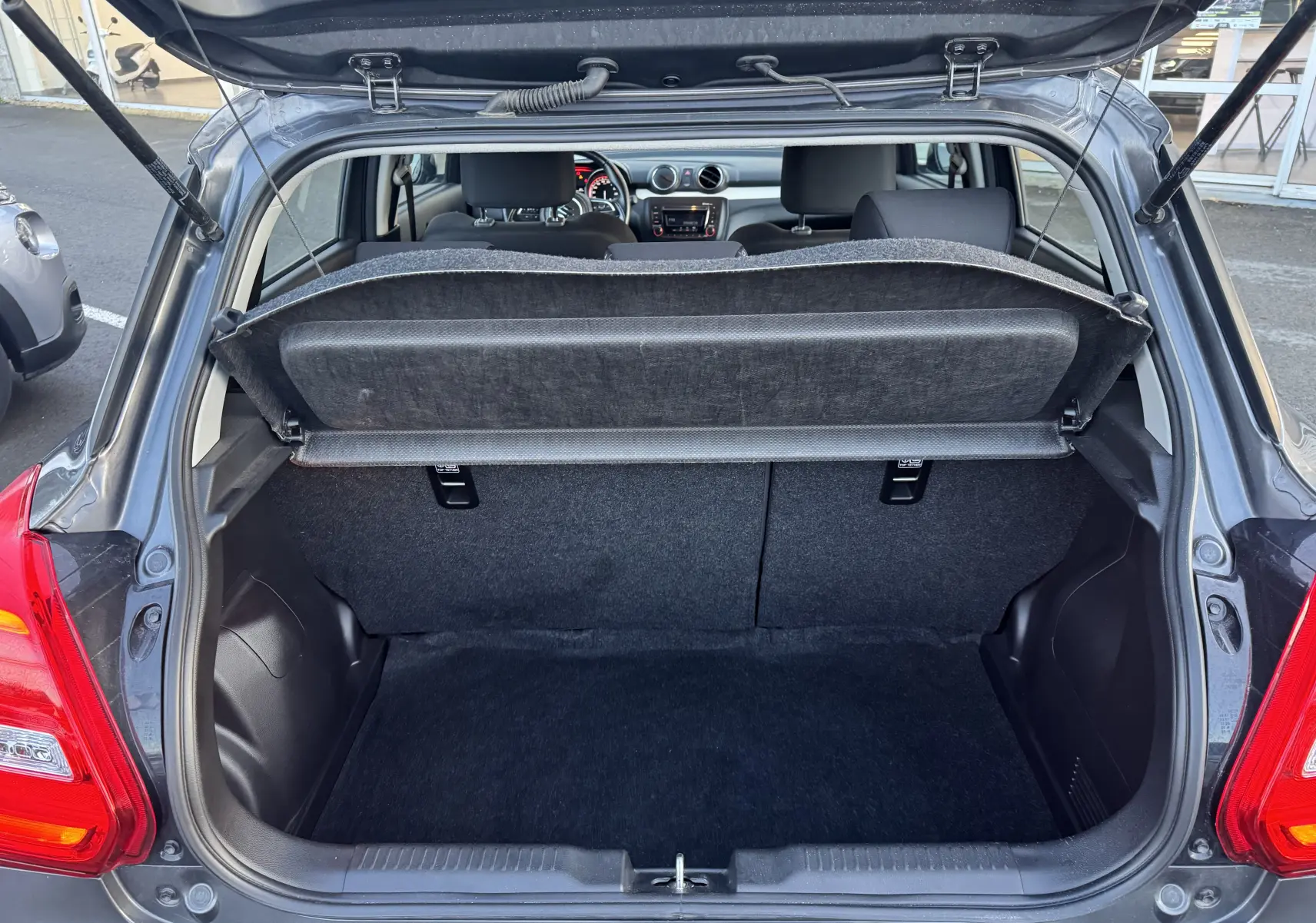 Vue arrière du coffre ouvert d'une Suzuki Swift 1.2 Dualjet Hybrid gris 2021, montrant l'intérieur et la tablette cache-bagages.