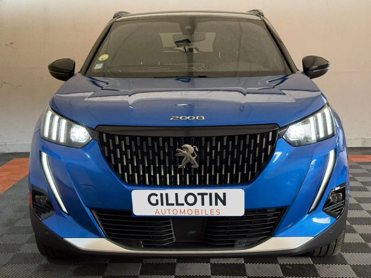 Vue avant d'un Peugeot 2008 bleu avec phares LED allumés et calandre noire distinctive, en intérieur.