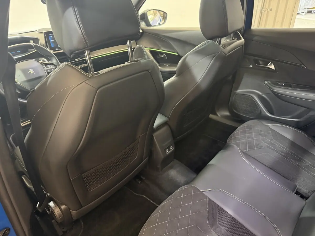 Vue intérieure arrière droite du Peugeot 2008 Bleu, sièges en cuir noir avec surpiqûres blanches et éclairage d'ambiance vert.