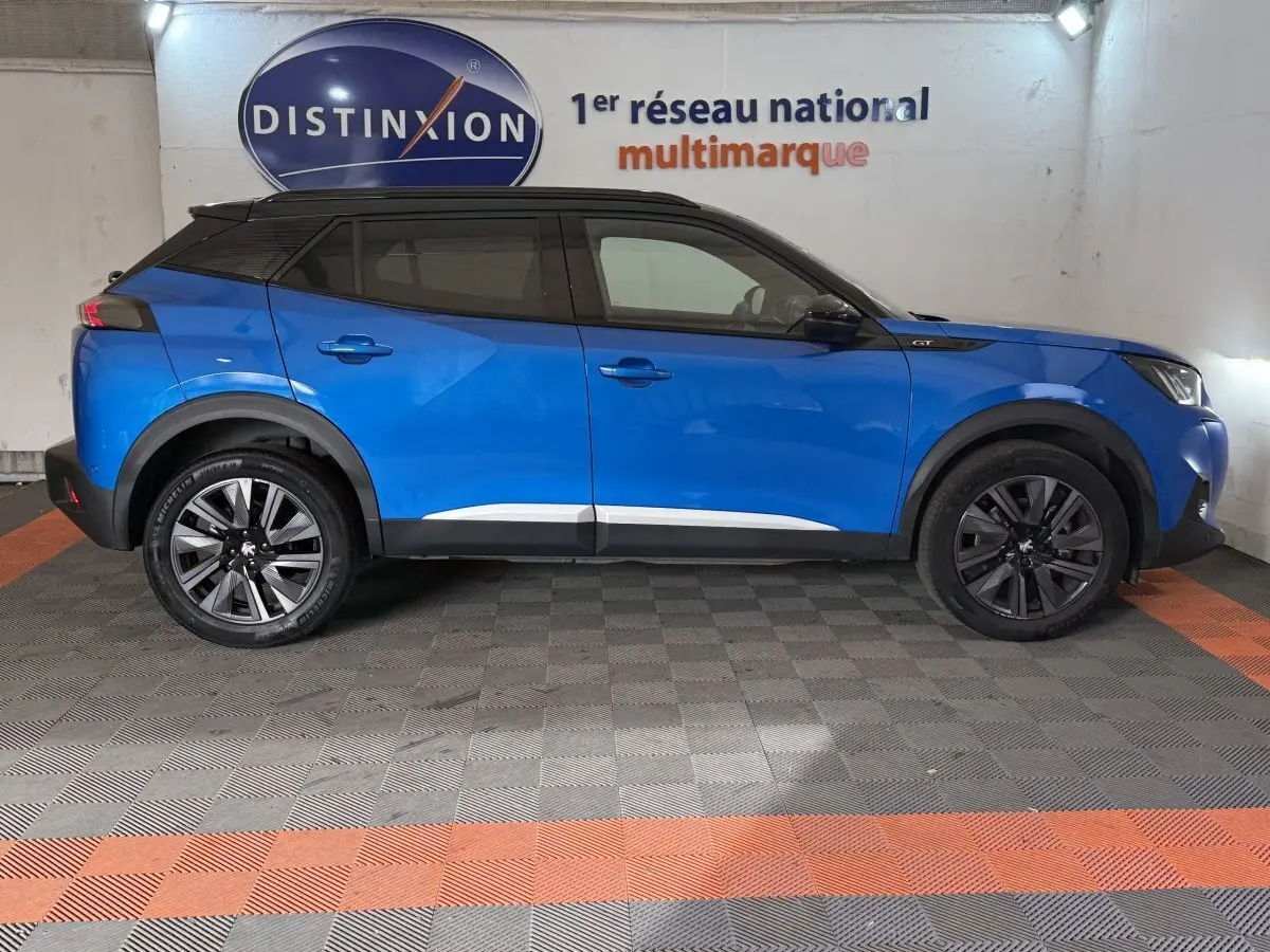 Peugeot 2008 bleu en profil droit, toit noir et jantes alliage, dans un showroom intérieur.