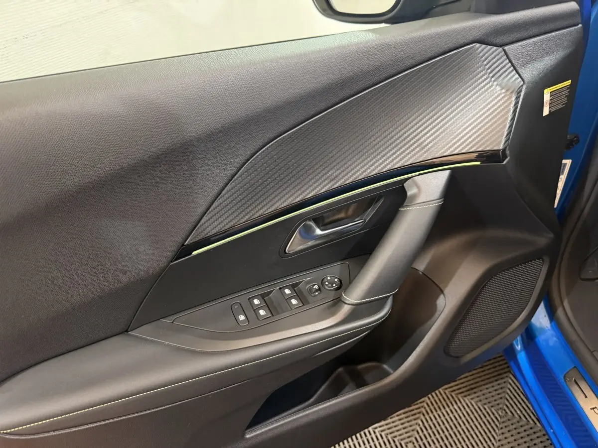 Vue rapprochée de la porte avant gauche bleu électrique du Peugeot 2008 GT Pack avec insert carbone et commandes électriques.