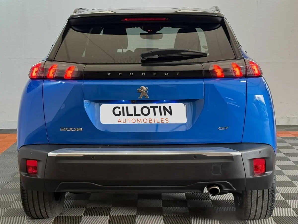 Vue arrière d’un Peugeot 2008 GT bleu avec feux LED allumés et logo Peugeot visible sur un sol carrelé.