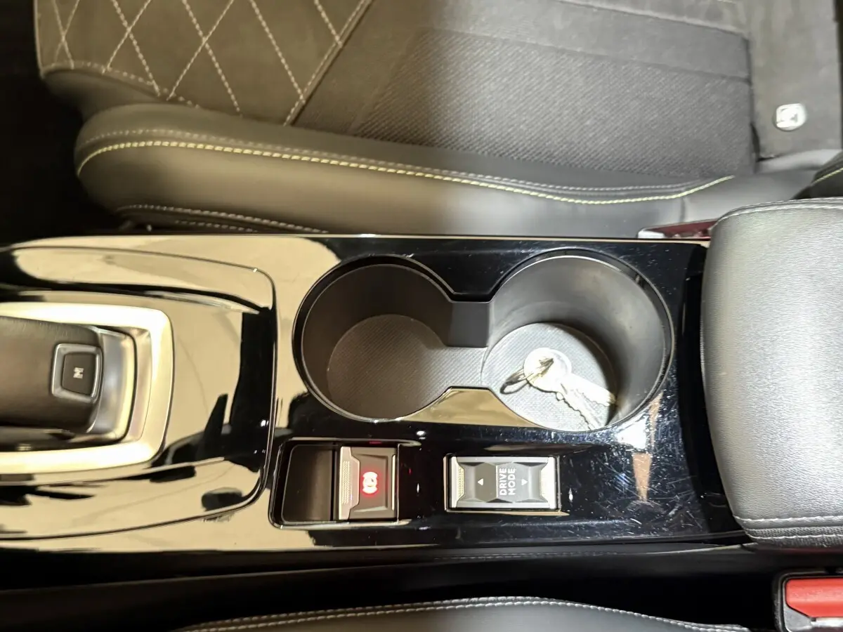 Vue rapprochée de la console centrale noire brillante du Peugeot 2008 GT Pack avec porte-gobelets et clés posées.